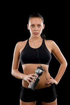 Sporty young woman posing with headphones and bottle black background