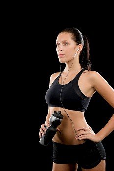 Sporty young woman with headphones and bottle on black background
