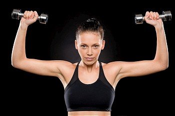 Attractive young brunette woman lifting dumbbells over her head pose