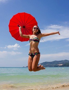 girl jumping on the beach with a red umbrella
