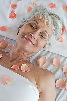 Senior woman covered in petals on bed