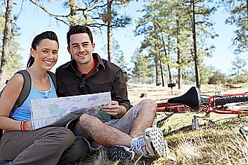 Young couple sitting outdoors reading map portrait.