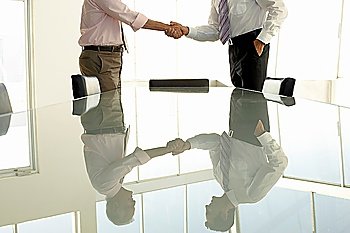 Businessmen shaking hands by conference table mid section