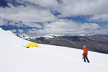 Hiker walking toward tent in snowy mountains