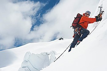 Mountain climber going up snowy slope with axes