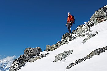 Mountain climber descending snow and boulder slope