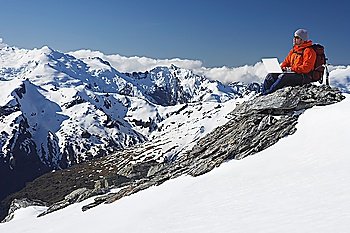 Mountain climber using laptop on mountain peak