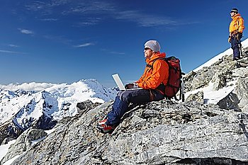 Mountain climber using laptop on mountain peak