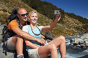 Man hugging woman as she takes their picture by a river in a forest