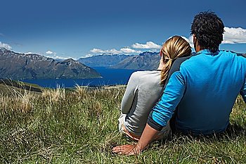 Couple cuddling looking over lake and hills back view