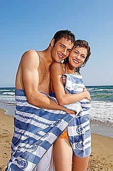 Young couple on beach wrapped in towel, portrait