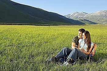Young couple sitting in mountain field looking at view, full length