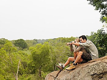 Man and woman sitting on rock looking at view man pointing