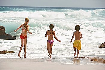 Three children (5-6 7-9 10-12) running on beach back view