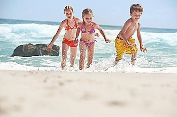 Three children (5-6 7-9 10-12) running on beach