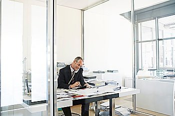Businessman sitting at desk in office talking on phone.