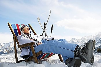 Female skier resting on deckchair in mountains