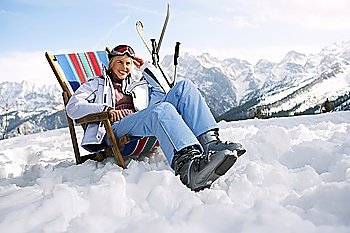 Female skier sitting on deckchair in mountains