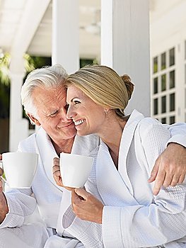 Couple sitting on verandah holding coffee cups