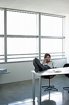 Business man using mobile phone sitting at office desk with feet up
