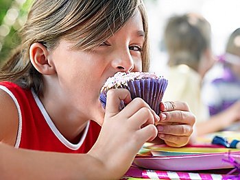 Girl (10-12) eating cupcake at birthday party