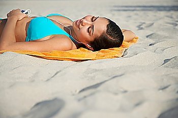 Teenage girl (16-17) using mp3 player lying on beach