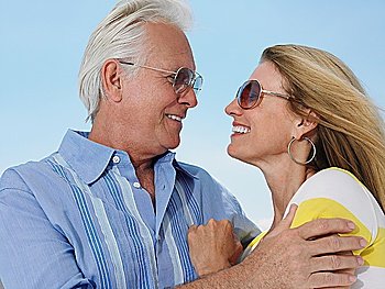 Middle-aged couple embracing and looking in eyes against sky