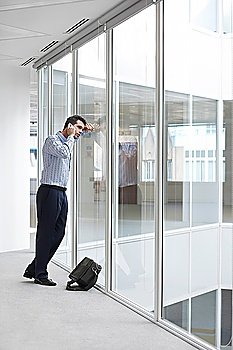 Office worker talking on mobile phone looking out window of empty office space