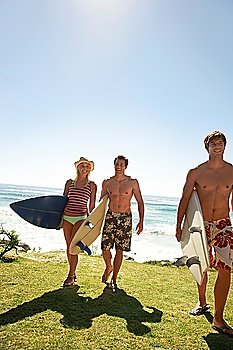 Three young people with surf board walking away from sea full length