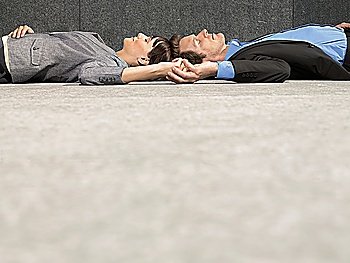 Business man and woman lying on ground head to head holding hands side view