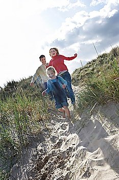 Parents and daughter (5-6) running through sand dunes