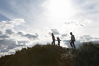Silhouette of parents and daughter (5-6) walking on sand dunes