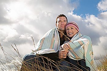 Couple wrapped in blanket embracing in grass