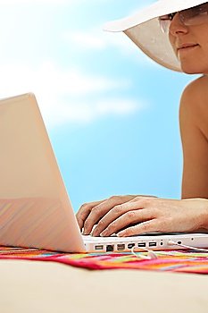 Woman using laptop lying on stomach on beach close up