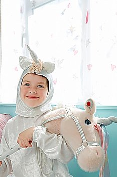 Portrait of young girl (5-6) in unicorn costume holding toy horse smiling indoors