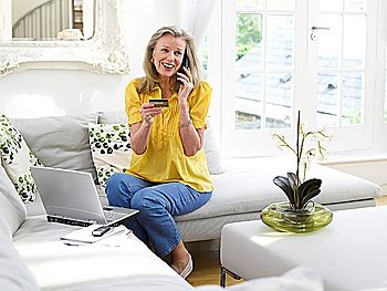 Woman holding credit card using phone in living room elevated view