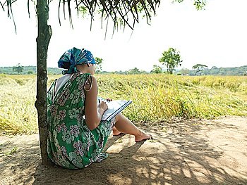 Young woman sitting in shade writing back view