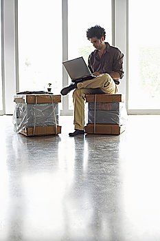 Man Sitting on Package Using Laptop