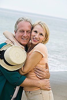 Middle-aged couple embracing on beach and looking at camera