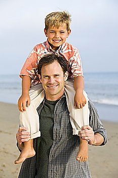 Portrait of boy on fathers shoulders at beach