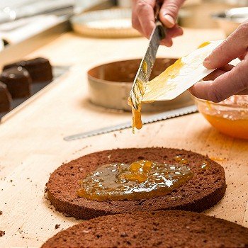 Cook making layer chocolate cake with orange marmalade