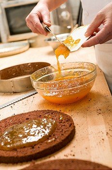 Chef pouring apricot jam to glass bowl making cake
