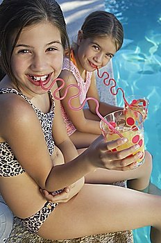 Girls drinking juice from crazy straws on edge of swimming pool, portrait