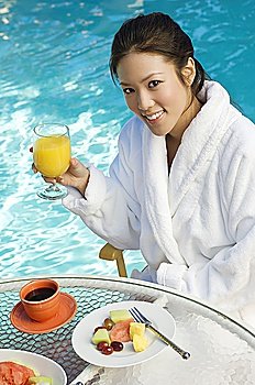 Young Chinese woman drinking orange juice by swimming pool, portrait
