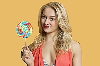Portrait of a young blond woman holding lollipop over colored background