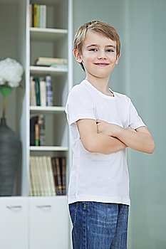 Portrait of little boy in casuals standing with arms crossed at home