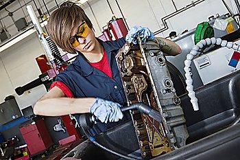 Young female mechanic working with welding torch on vehicle machinery part in auto repair shop