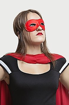 Young woman in superhero costume looking up over gray background