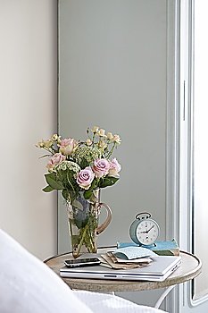 Roses in vase on bedside table with books and alarm clock