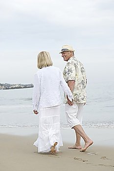 Senior couple walk holding hands on beach